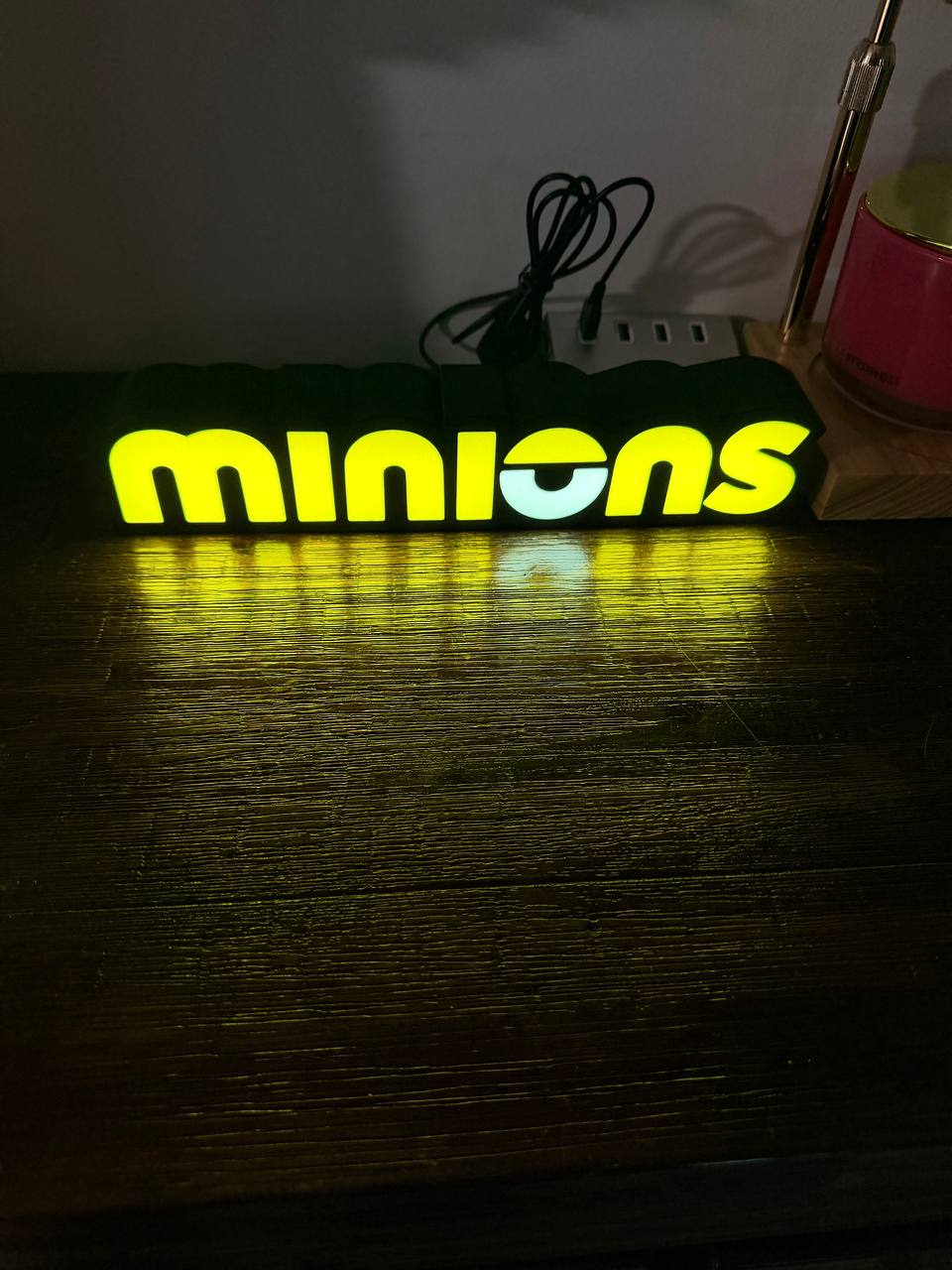 Minions LED light-up sign glowing yellow on wooden desk — front view