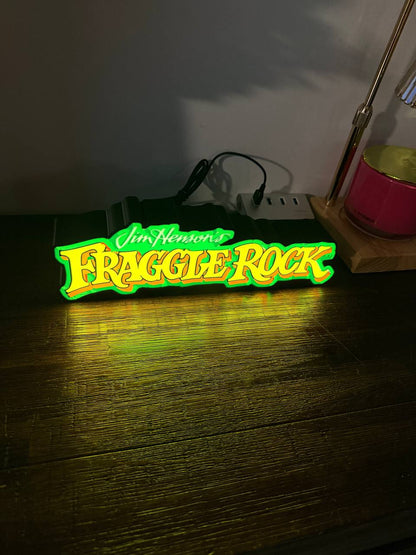 Fraggle Rock LED light-up sign glowing yellow and orange on wooden desk — front view
