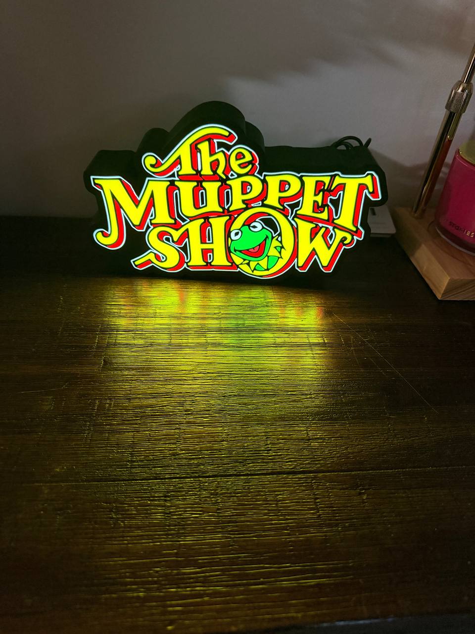 The Muppet Show LED light-up sign glowing on wooden desk — front view